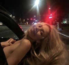 a woman sitting in the driver's seat of a car at night with traffic lights behind her