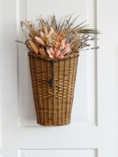 a wicker basket hanging on the front door with dried flowers in it and foliage