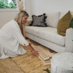 a woman kneeling down on the floor in front of a couch with pillows and rugs