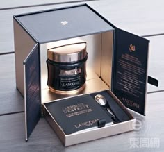 an open box with a candle inside on a wooden floor next to it is a black and gold package