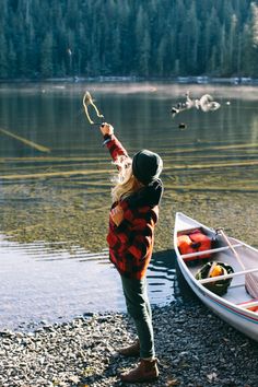 a woman standing next to a boat on top of a lake holding a fishing pole