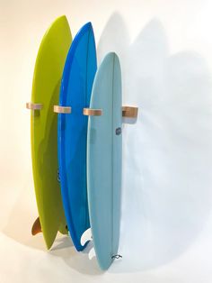 three surfboards are lined up against the wall and one is blue, green, and yellow