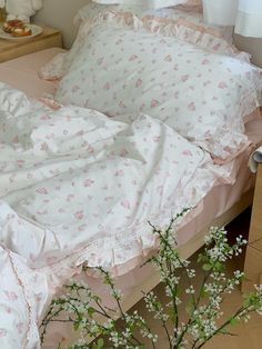 an unmade bed with pink and white flowers on the pillowcase, next to a dresser