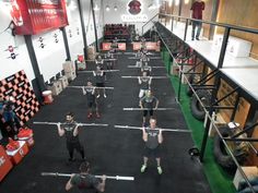 a group of people doing exercises with barbells in an indoor gym area while others watch