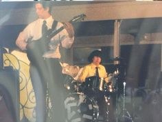 a man playing the drums while standing next to another man on stage in front of him