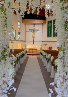 an aisle decorated with white flowers and greenery in front of a church pews