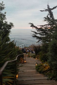 a wooden path leading to the ocean with people sitting on it and candles lit up