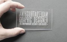 a person holding up a clear plastic business card with the word graphic designer printed on it