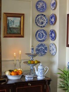 blue and white plates are hanging on the wall above a buffet table with fruit, vegetables, and candles