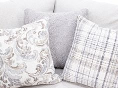 three pillows are sitting on the back of a gray couch with white and blue accents