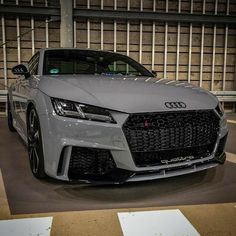 the front end of a grey sports car parked in a parking lot next to a building