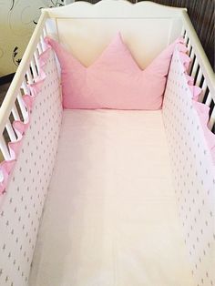 a white crib with pink sheets and pillows