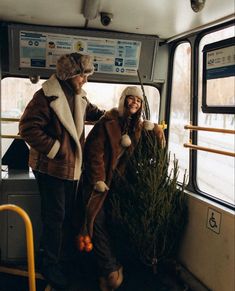 two people standing next to each other on a bus with christmas trees in their hands