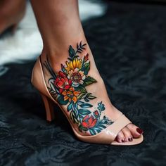 a woman's foot with tattoos on it and flowers on the heel, while she is wearing high heels