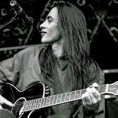 a man with long hair playing an acoustic guitar