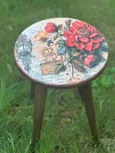 a small wooden stool with flowers painted on the top and bottom, sitting in grass