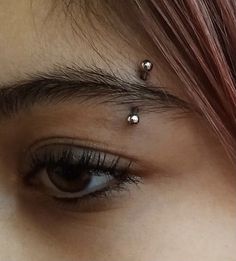 a close up of a person's eye with some piercings on their forehead