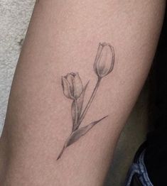 a black and white photo of a flower tattoo on the right thigh, with two tulips growing out of it