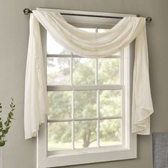 a window with white drapes hanging from it's side in front of a gray wall