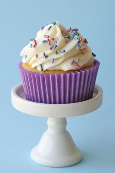 a cupcake with white frosting and sprinkles on a cake stand