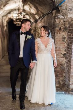 a bride and groom holding hands while walking through an old brick tunnel in their wedding attire