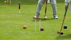 two men are playing croquet golf on the green grass in front of several balls