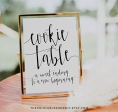 a cookie table sign sitting on top of a wooden table next to a white feather