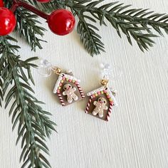 two christmas themed earrings hanging from a pine branch