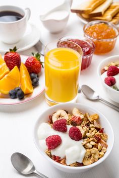 an assortment of breakfast foods including fruit, yogurt, granola and orange juice