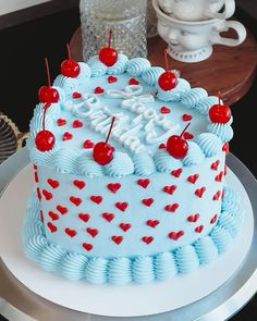 a blue and white cake with cherries on it sitting on top of a table