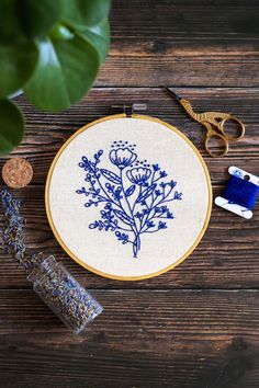 a blue and white embroidered flower on a wooden table next to scissors, thread, and spools of thread