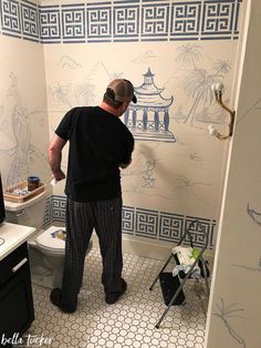 a man in black shirt and plaid pants painting a wall with blue and white designs