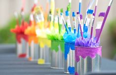 colorful toothbrushes are lined up in tins on a gray tablecloth outdoors