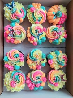 cupcakes in a box decorated with colorful icing and flower decorations on top