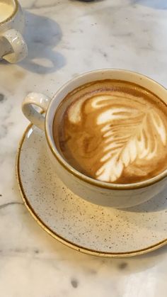 a cappuccino in a white cup and saucer on a marble table