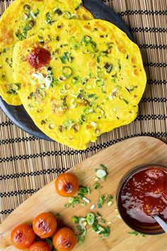 two omelets on a wooden cutting board next to some sauce and small oranges