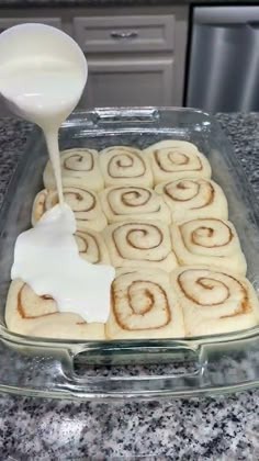 a pan filled with cinnamon rolls and cream being drizzled on top of it