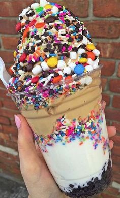 a person holding an ice cream sundae with sprinkles and toppings