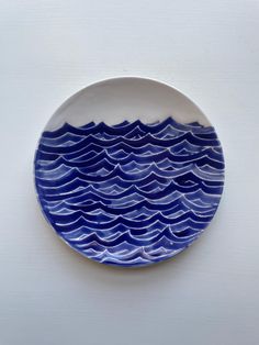 a blue and white plate sitting on top of a table next to a wall with an ocean wave painted on it