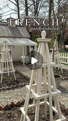 a wooden garden obelisk sitting on top of gravel next to a white fence