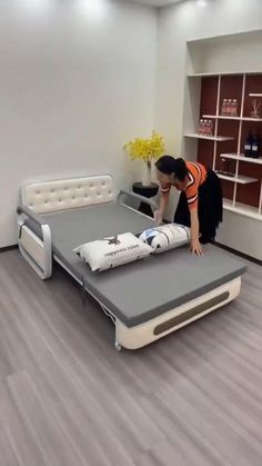 a man standing over a bed that is in a room with wood floors and white walls