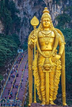 a large golden statue stands in front of stairs leading up to the top of a mountain