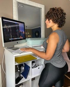 a woman standing in front of a computer desk with a monitor and keyboard on it