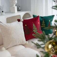 three christmas pillows sitting on top of a couch next to a christmas tree and other decorations