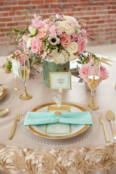 the table is set with gold and white plates, silverware, and pink flowers