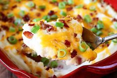 a spoonful of mashed potatoes with bacon and green onions on top, in a red casserole dish