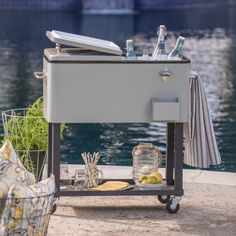 a cooler sitting on top of a table next to a body of water with bottles and lemons