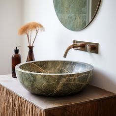 a marble bowl sink sitting on top of a wooden counter next to a round mirror