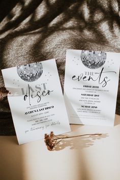 two white cards with black lettering on them sitting on a table next to a flower