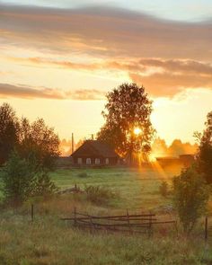 the sun is setting over an open field with a farm house in the foreground